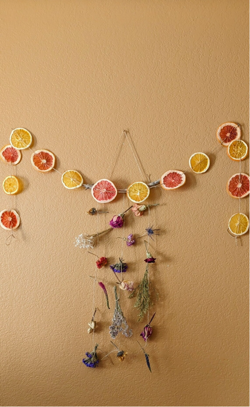 Decorative citrus wall hanging with dried fruits and flowers on a warm toned wall